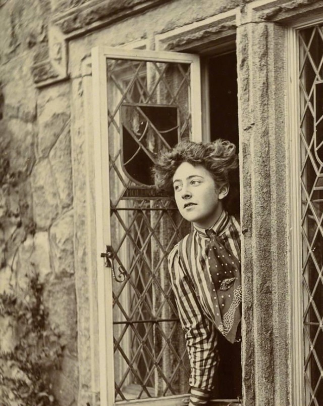 black and white photograph of young woman leaning out of window.