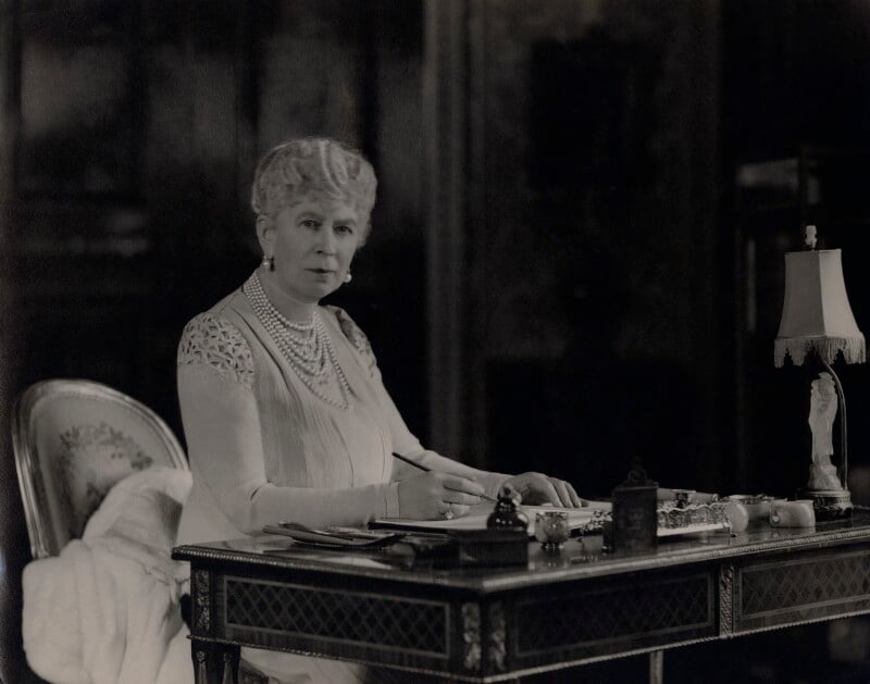 black and white photograph of queen Mary sitting at a writing desk.