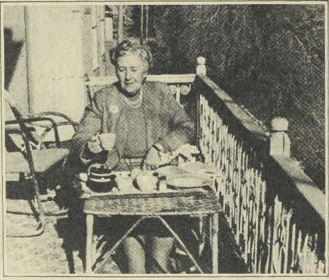 photograph of Agatha in 1950s sitting at a table on a balcony having breakfast. She is holding a cup of tea.