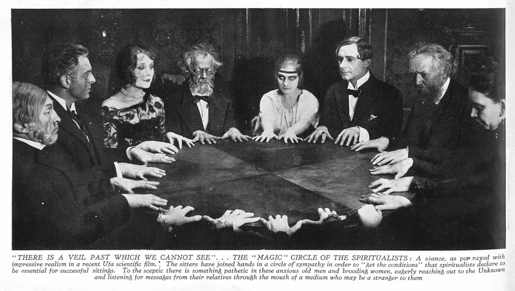 group sitting around a table holding a seance.